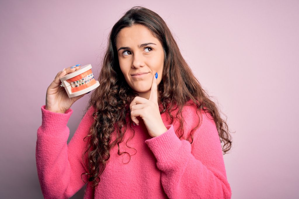 Posada de mujer una sudadera rosa sosteniendo un molde dental, mirando curioso