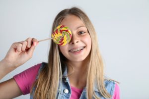 niña sonriente con aparatos ortopédicos sosteniendo una piruleta