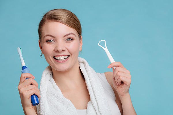 Mujer sosteniendo un cepillo de dientes eléctrico y un limpiador de lengua.